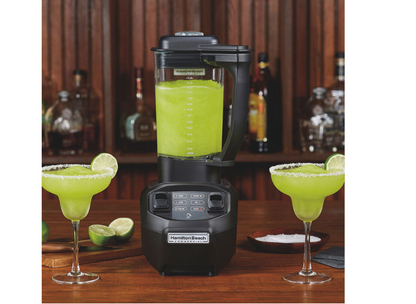 Blender full of cocktail mixture next to two cocktails